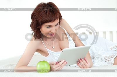 Mujer con una manzana verde y una tableta en la cama | Foto de alta resolución |ID 3666229